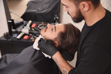 Professional hairdresser using cold towel to calm client's skin after shaving in barbershop