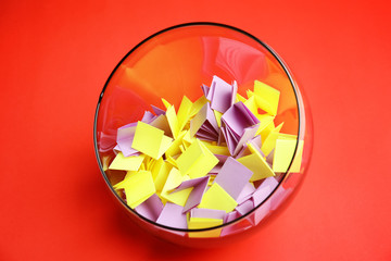 Paper pieces for lottery in glass vase on color background