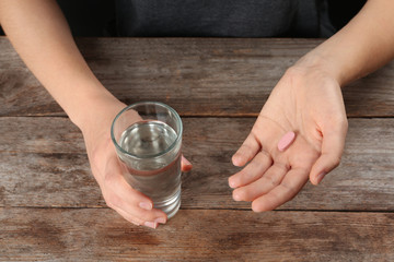 Fototapeta na wymiar Woman holding pill and glass of water at table, closeup