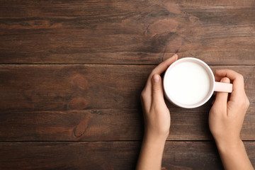 Woman holding cup of milk on wooden table, top view. Space for text