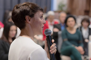 Beautiful business woman with microphone in her hand speaking at the  conference or seminar.
