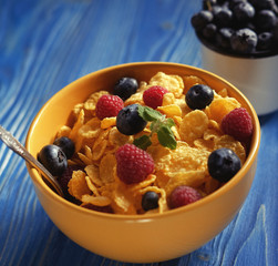 Cornflakes with berries raspberries and blueberries on blue wooden background.