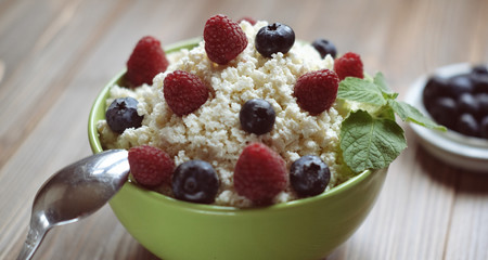 Cottage cheese in green bowl with raspberries and blueberries on wooden background. Healthy Breakfast.