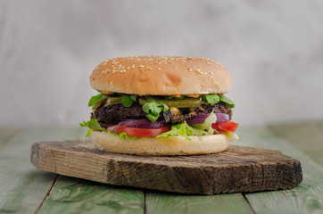 Delicious homemade burger with beef, tomatoes, lettuce and cheese on wood cutting board close up