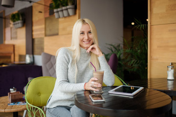Reading Concept. Young blond Woman using Tablet or e-book and Drinking Coffee. Relaxing in Cozy cafe, Sit on the Chair