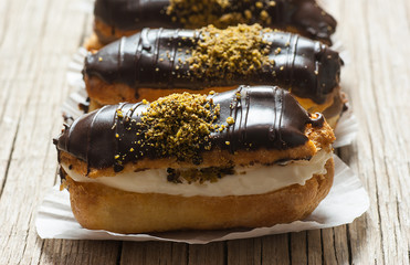 Eclairs with pistachio and black chocolate and white chocolate with custard on wooden background and backdrop. Traditional French dessert. Eclair Pastery concept