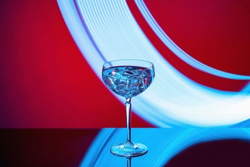 Beautiful view of alcohol drink with ice cubes in crystal glass on colorful background. 