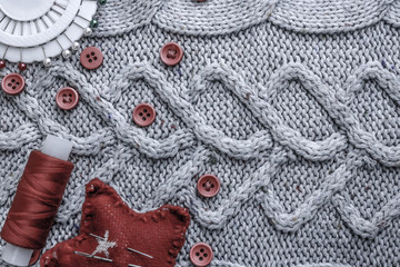 Beautiful texture of a soft warm natural sweater, fabrics with a knitted pattern and red small round buttons for sewing and a skein of thread, needle bed and needle pad. Flat lay. The background