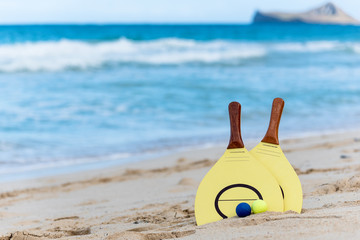 Obraz premium Yellow beach paddle and balls on a sandy beach in Hawaii with waves and an island in the background