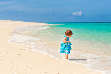Fototapeta na wymiar Cute baby in blue dress walking on the beach with white sand on the shore of the turquoise ocean. Boracay. Philippines
