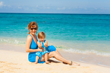 Mother with her Cute baby in blue dress having fun on the white sand beach on the shore of the turquoise ocean. Boracay. Philippines. Family vacation