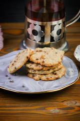 Homemade chocolate chip cookies on a beautiful saucer, kettle of tea, on a wooden dark background