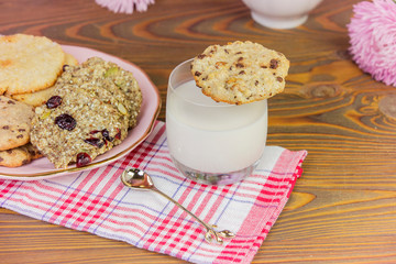 Homemade cookies: coconut, oatmeal, chocolate, on a wooden table, with a glass of milk, against the background of a summer composition with flowers