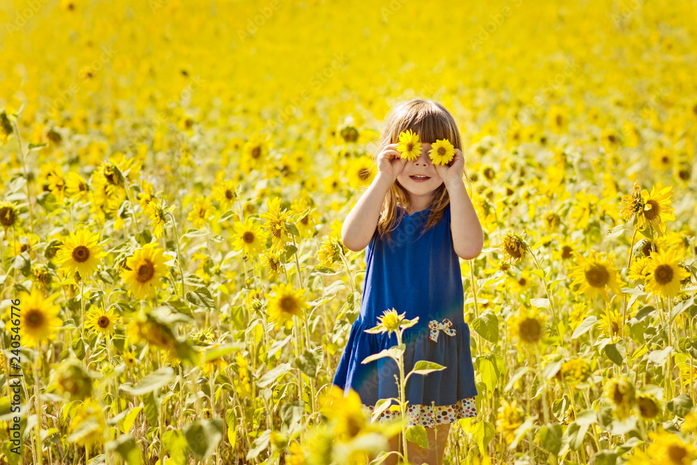 Wall mural happy little girl with fun playing among the blooming sunflowers, closing her eyes with flowers