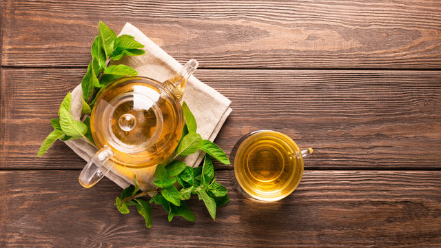 Fragrant fresh herbal tea of ​​mint and melissa in a glass cup and a teapot on a dark wooden background. Traditional herbal drink. Place for text or design. Flat layout. View from above.