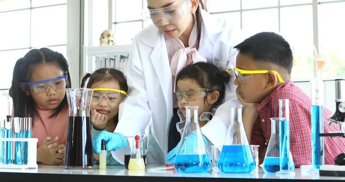 Science teacher teach Asian students, teacher pouring purple liquid to beaker and drop something into beaker, colorful test tube and microscope on table , concept for study in laboratory room.