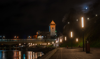 Fototapeta na wymiar Night view of Narva castle with the tower of High Herman, Narva, Estonia. The castle is illuminated. In the foreground is the city promenade. Opposite Narva is the Russian city of Ivangorod