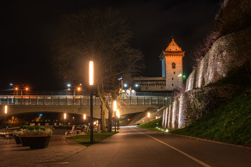 Fototapeta na wymiar Night view of Narva castle with the tower of High Herman, Narva, Estonia. The castle is illuminated. In the foreground is the city promenade. Opposite Narva is the Russian city of Ivangorod