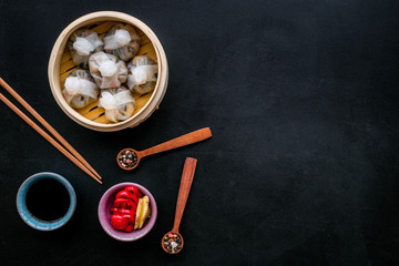 Dim sums with red pepper and vegetables with sticks and black tea in Chinese restaurant on black background top view mockup