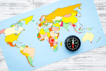 travel direction and trip planning concept with compass and map of the world on gray wooden background top view