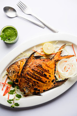 Tandoori Pomfret fish cooked in a clay oven and garnished with lemon , mint, cabbage and carrot salad. Selective focus