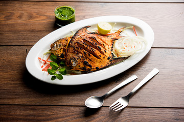 Tandoori Pomfret fish cooked in a clay oven and garnished with lemon , mint, cabbage and carrot salad. Selective focus