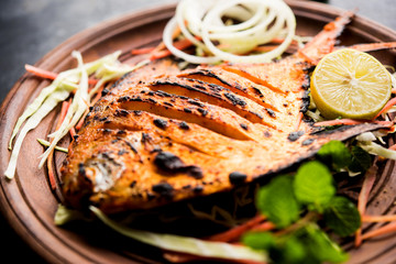 Tandoori Pomfret fish cooked in a clay oven and garnished with lemon , mint, cabbage and carrot salad. Selective focus