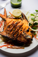 Tandoori Pomfret fish cooked in a clay oven and garnished with lemon , mint, cabbage and carrot salad. Selective focus