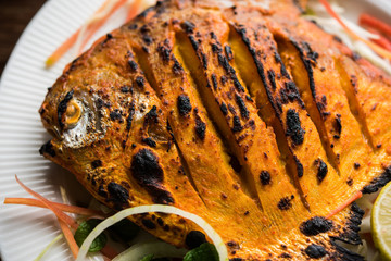 Tandoori Pomfret fish cooked in a clay oven and garnished with lemon , mint, cabbage and carrot salad. Selective focus