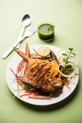 Tandoori Pomfret fish cooked in a clay oven and garnished with lemon , mint, cabbage and carrot salad. Selective focus
