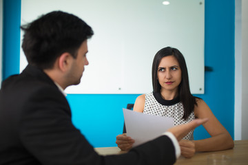 Young businesswoman looking at male partner with distrust during meeting. Male executive talking to female employee at briefing. Business relationships concept