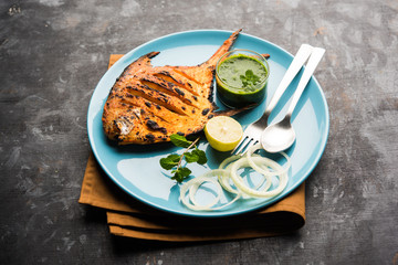 Tandoori Pomfret fish cooked in a clay oven and garnished with lemon , mint, cabbage and carrot salad. Selective focus