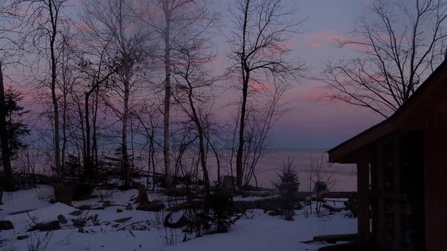 Dawn over Lake Superior in winter, Upper Peninsula, Michigan, seen through silhouetted trees on snowy shore. HD time lapse