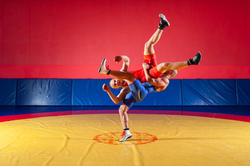 Two greco-roman  wrestlers in red and blue uniform making a suplex wrestling   on a yellow wrestling carpet in the gym. The concept of fair wrestling