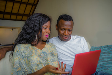 young happy and attractive black afro American couple together at home sofa couch networking with laptop computer banking online or internet shop relaxed and cheerful