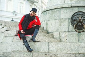 Portrait of a young beautiful fashionable woman in a red coat . Model posing on a city street