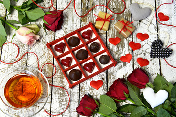 Top view with cup of tea, beautiful rose flowers, chocolate candies and gifts on planks. Romantic vintage valentine’s day and wedding background