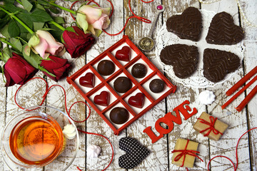 Top view of sweet candies, heart and love symbols, gifts, rose flowers on wooden planks. Romantic vintage valentine’s day and wedding background