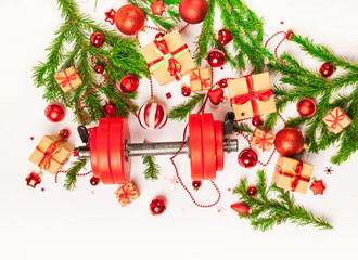 Christmas or New Year on a white background. Composition with dumbbells, gift, red and gold glass balls, fir tree branches for healthy lifestyle and sport