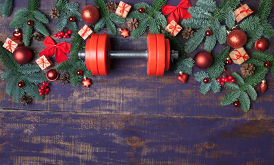 Christmas or New Year on a violet wooden background. Composition with dumbbells, gift, red and gold glass balls, fir tree branches for healthy lifestyle and sport