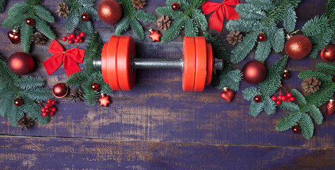Christmas or New Year on a violet wooden background. Composition with dumbbells, gift, red and gold glass balls, fir tree branches for healthy lifestyle and sport