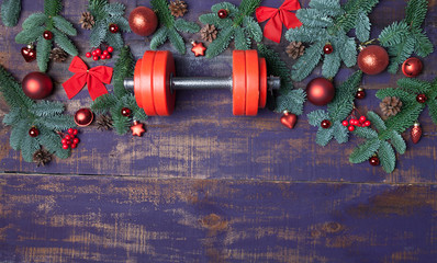 Christmas or New Year on a violet wooden background. Composition with dumbbells, gift, red and gold glass balls, fir tree branches for healthy lifestyle and sport