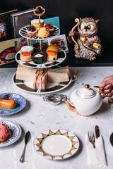 English afternoon tea set including hot tea, pastry, scones, sandwiches and mini pies on marble top table.