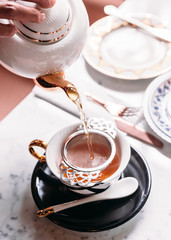 Hot Apple Tea served by pouring from mug through stainless steel tea strainer infuser in porcelain vintage cup.