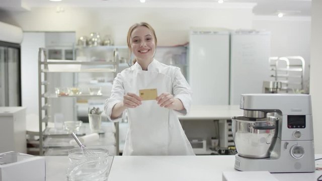 Portrait of a happy young sous chef lady or worker in a commercial kitchen. Woman is posing in the kitchen. Showing payment card