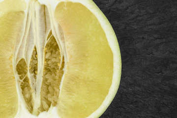 Close-up background surface view of cut pomelo fruit on black stone background surface and copy...