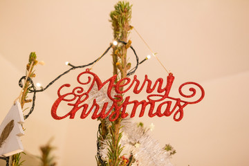 Ozdoby choinkowe - napis merry christmas zawiszony na choince zdobionej lampkami - święta