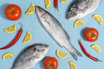 Raw dorada fish with spices, salt, lemon and herbs, rosemary on a ligth-blue background. Top view.