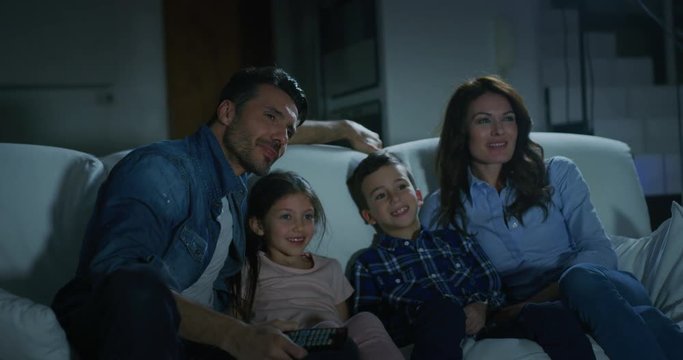 Portrait of happy family watching TV on sofa in the evening in living room in slow motion. Shot with RED camera in 8K. Concept of family entertainment, education, technology.