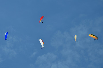 Paragliders are circling in an ascending current above the mountain Sarangkot. Blue sky, multi-colored wings.
